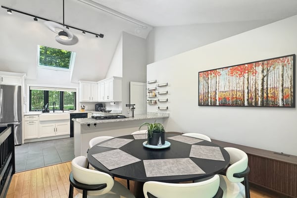 Modern kitchen and dining area with white cabinetry, black round table with cream chairs, and forest artwork on wall