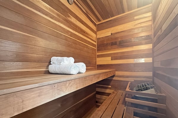 Interior of wooden sauna with bench, rolled white towels, and heating element below