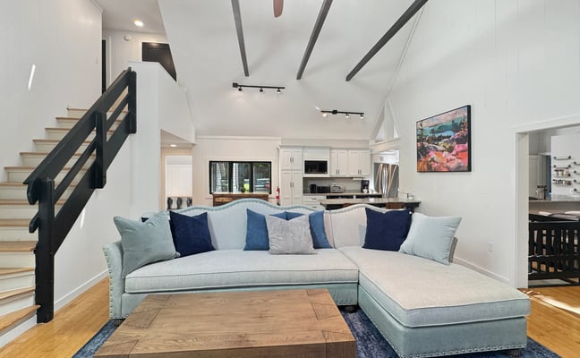 Open-plan living room with light blue sectional sofa, wooden coffee table, black staircase, and kitchen visible in background
